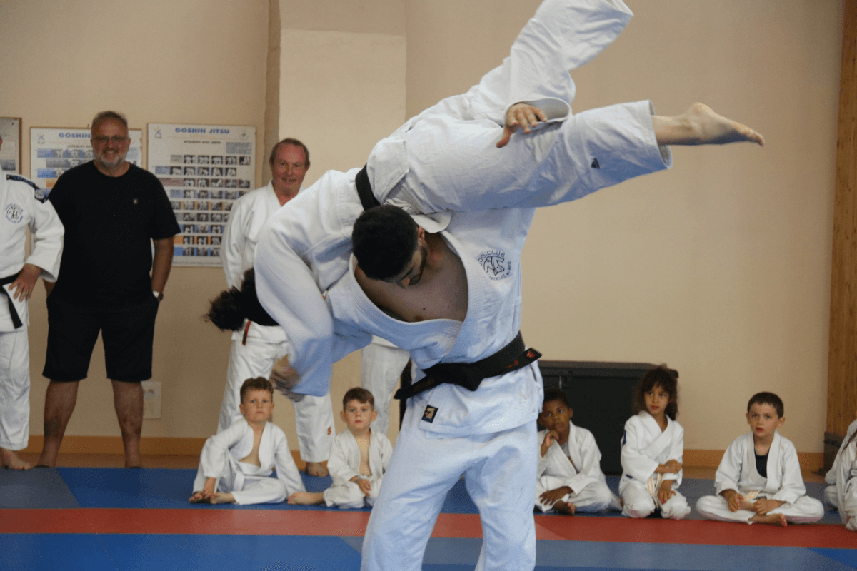 Un instructeur de judo remettant une ceinture à un jeune garçon en présence d'autres membres du dojo.