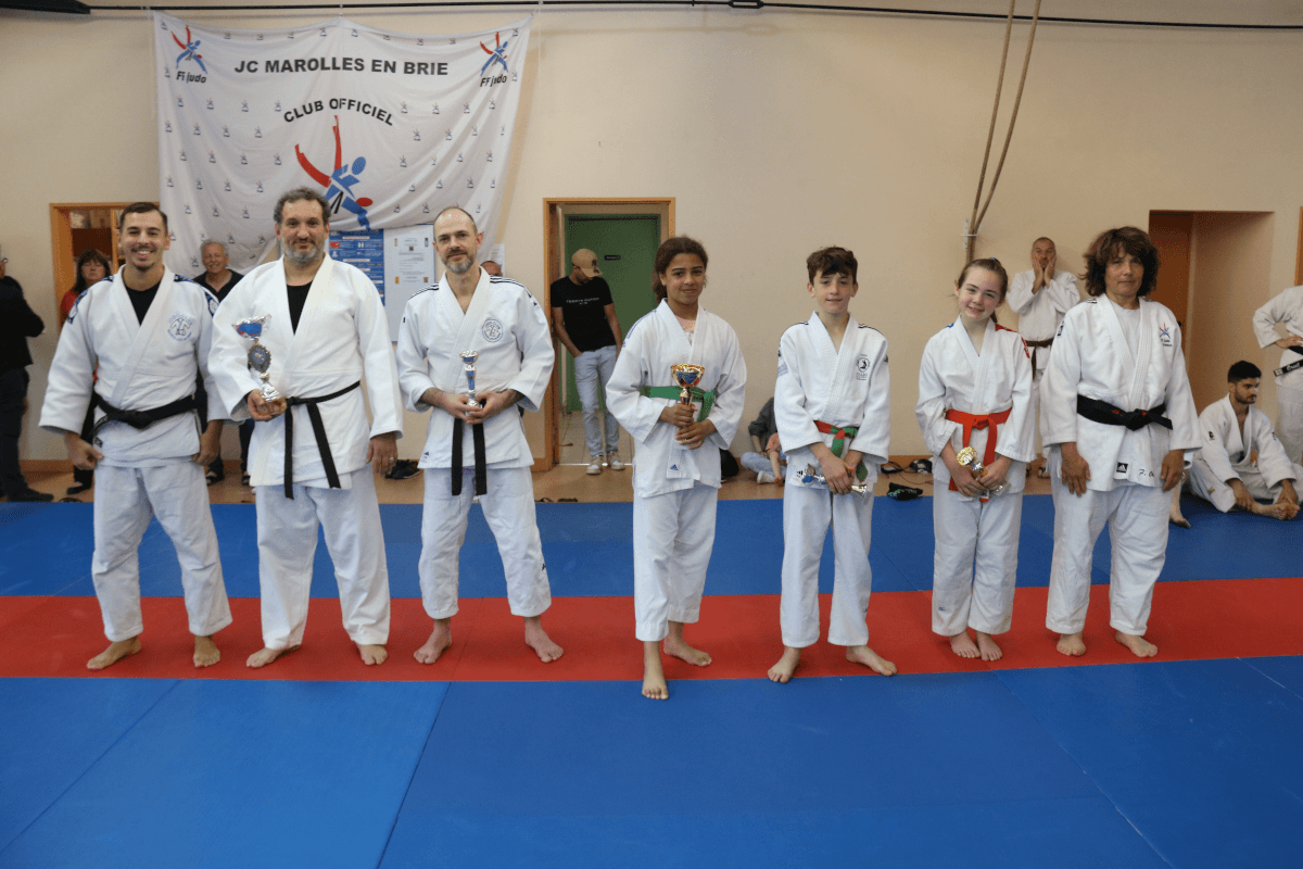 Les familles et les judokas posent ensemble pour une grande photo de groupe en levant les mains pour célébrer la fin d'un événement de judo.