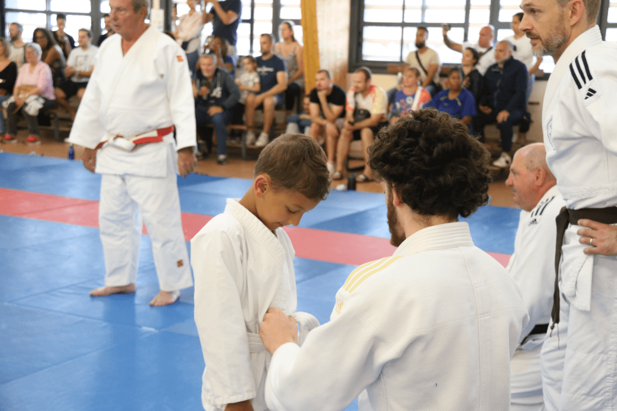 Un jeune judoka se préparant à recevoir sa nouvelle ceinture lors d'une cérémonie en présence de ses camarades et des parents.