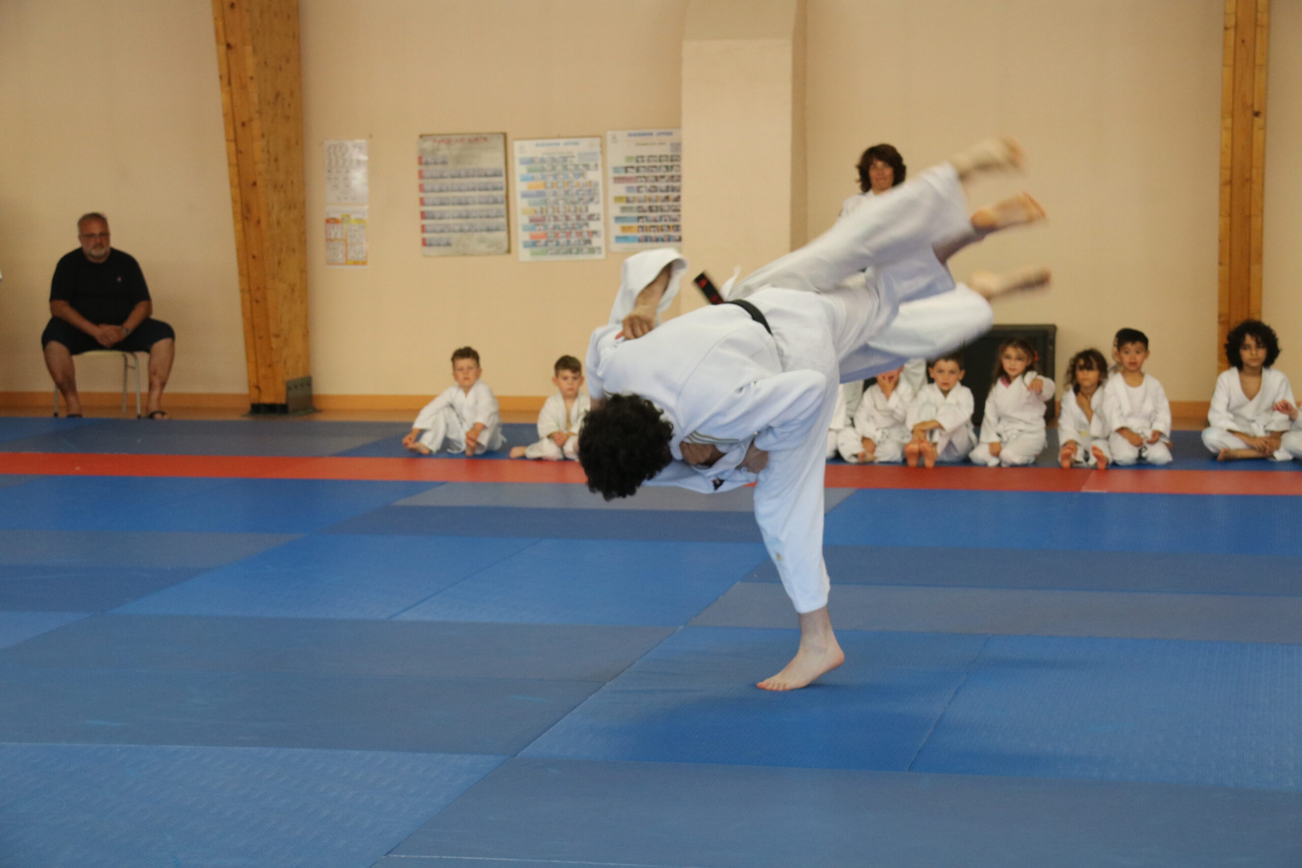 Des enfants alignés en tenue de judo, attendant leur tour pour une activité, avec des ceintures colorées exposées devant eux.