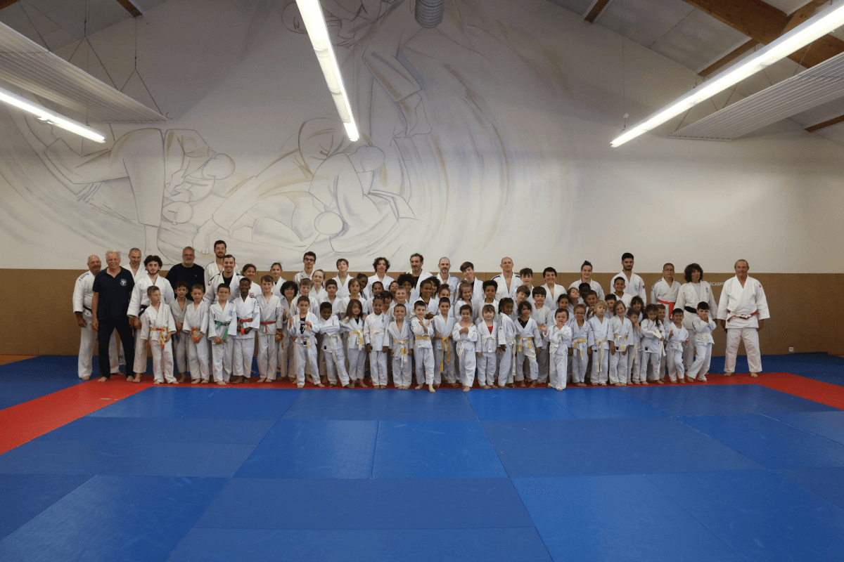 Un pratiquant de judo exécutant un mouvement de projection pendant une démonstration au dojo sous le regard des enfants assis.