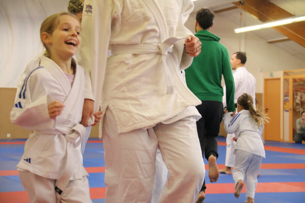 Deux judokas exécutant une technique de projection, sous le regard attentif de jeunes enfants assis au fond.