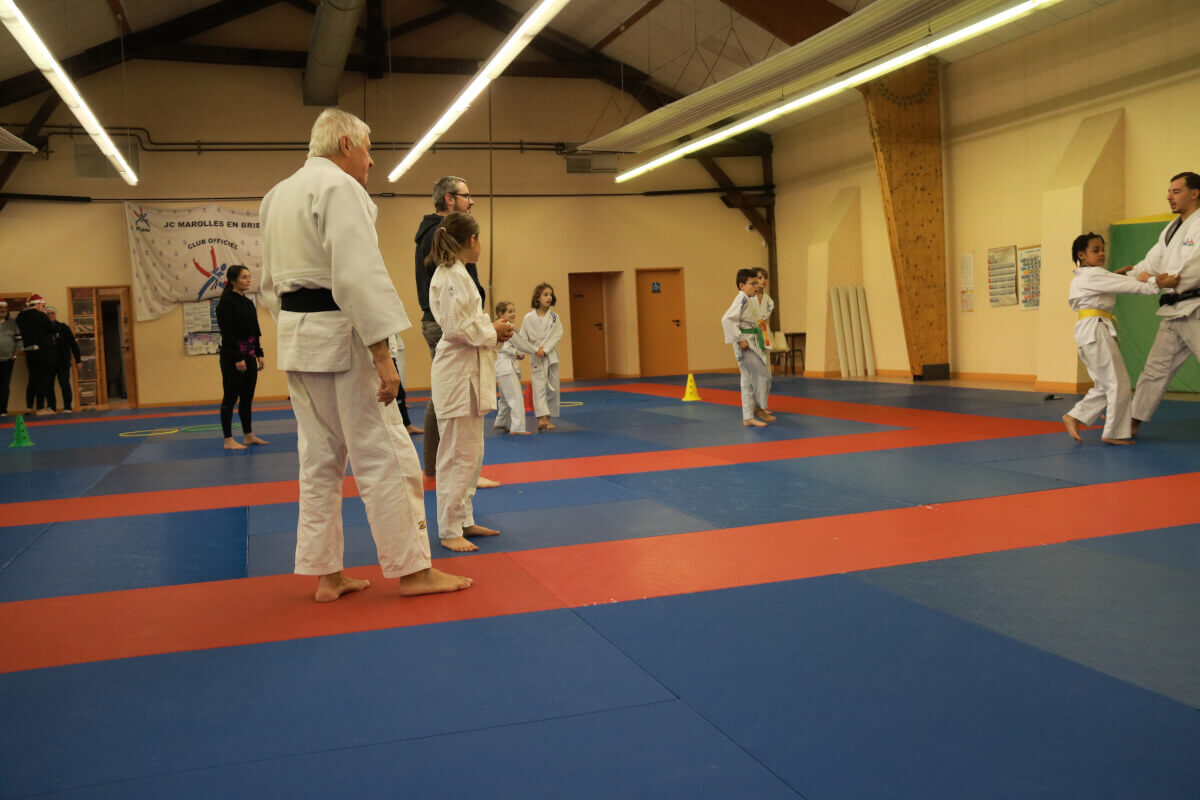 Un instructeur de judo remettant une ceinture à un jeune garçon en présence d'autres membres du dojo.