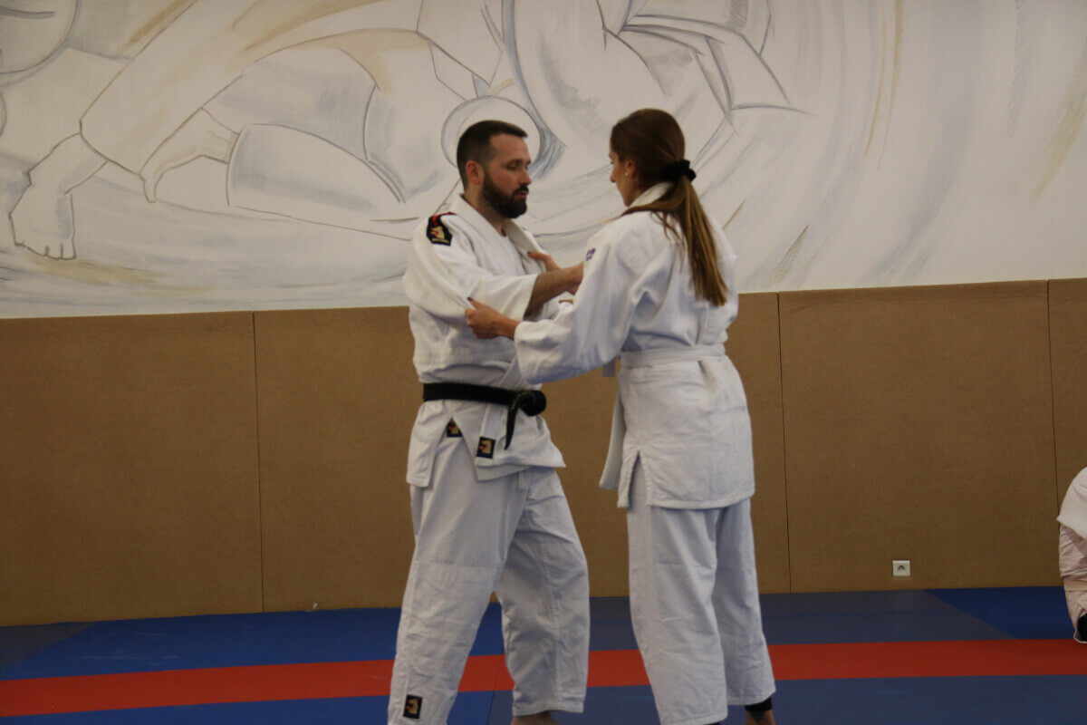 Judokas alignés avec leurs trophées, de différents âges, lors d'une remise de récompenses au dojo.