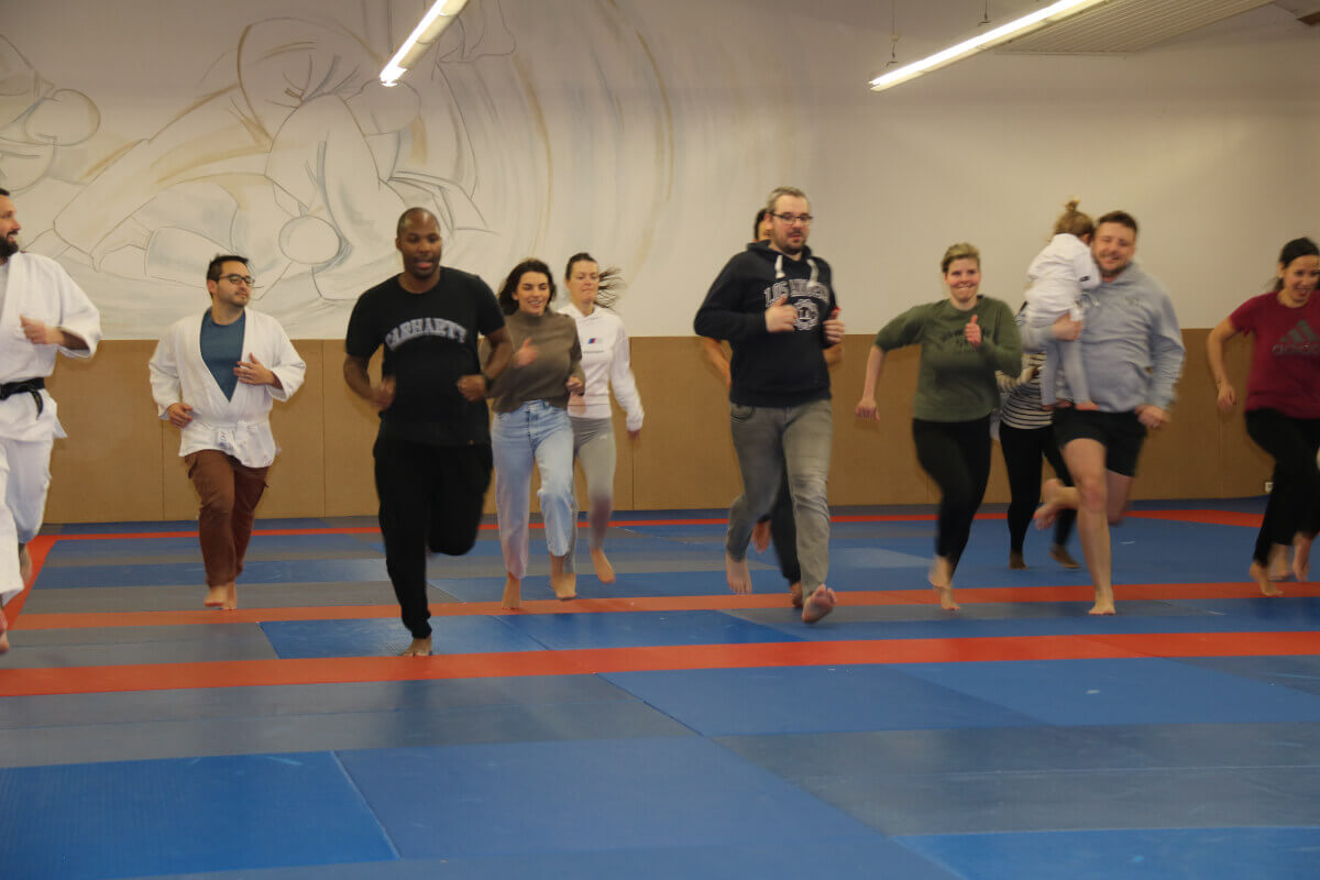 Les familles et les judokas posent ensemble pour une grande photo de groupe en levant les mains pour célébrer la fin d'un événement de judo.