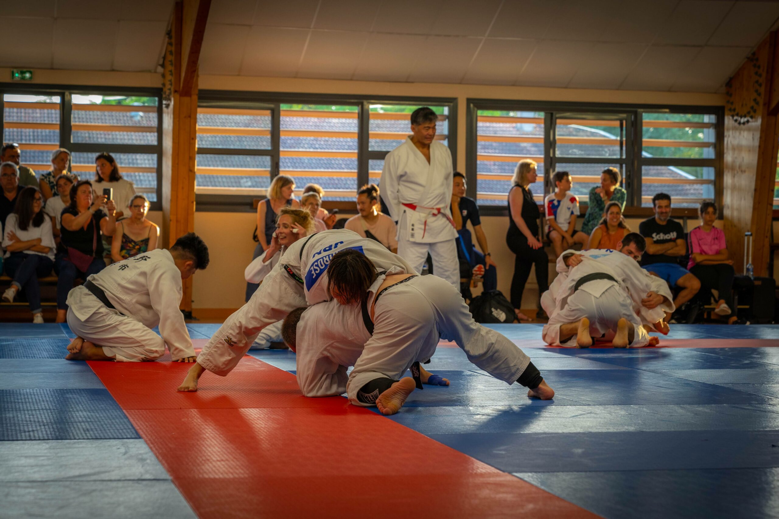 Judokas s'entraînant en groupe, sous l'œil des coaches et spectateurs.