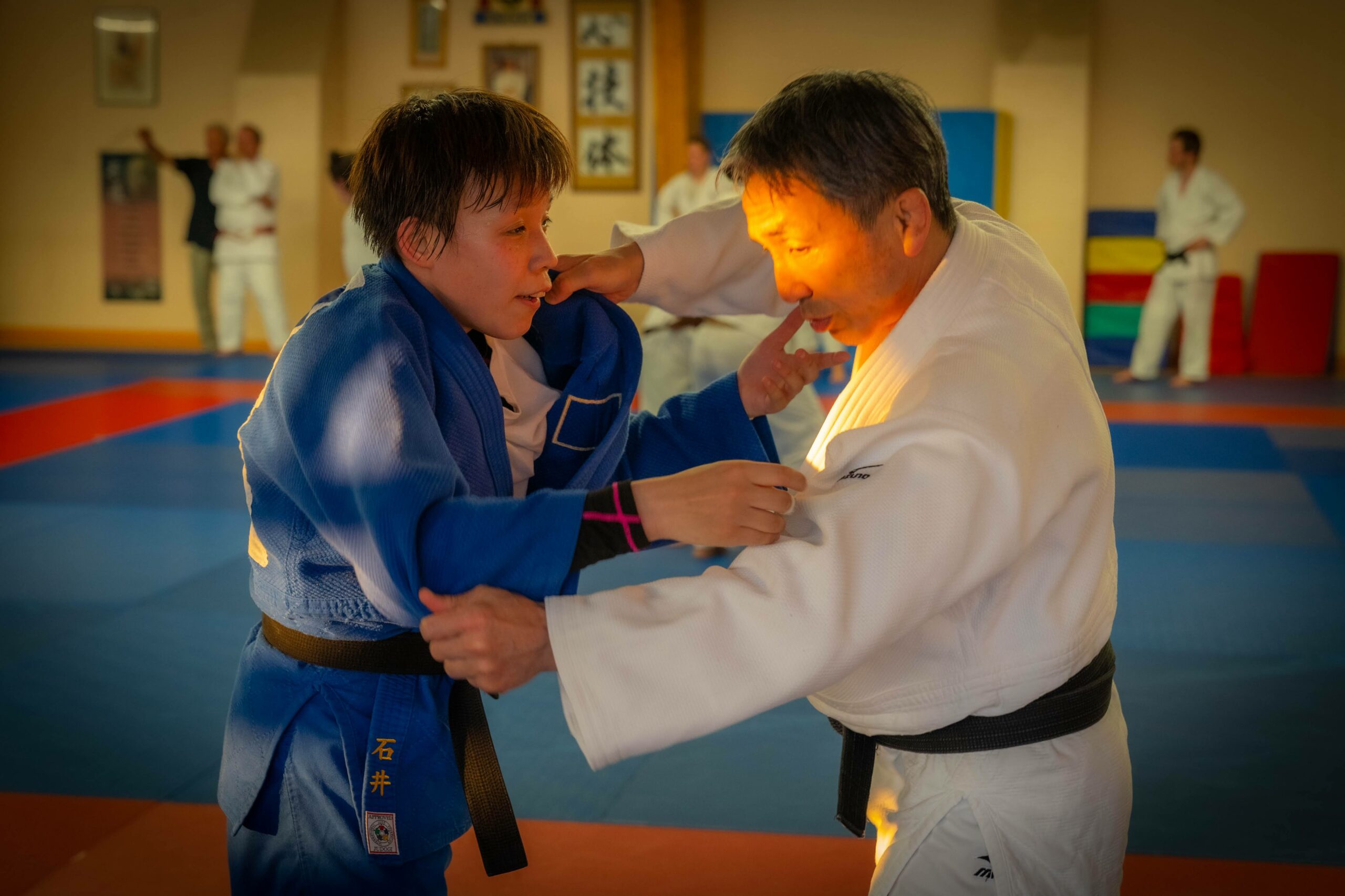 Deux judokas, l'un en gi bleu, effectuant un exercice de saisie.