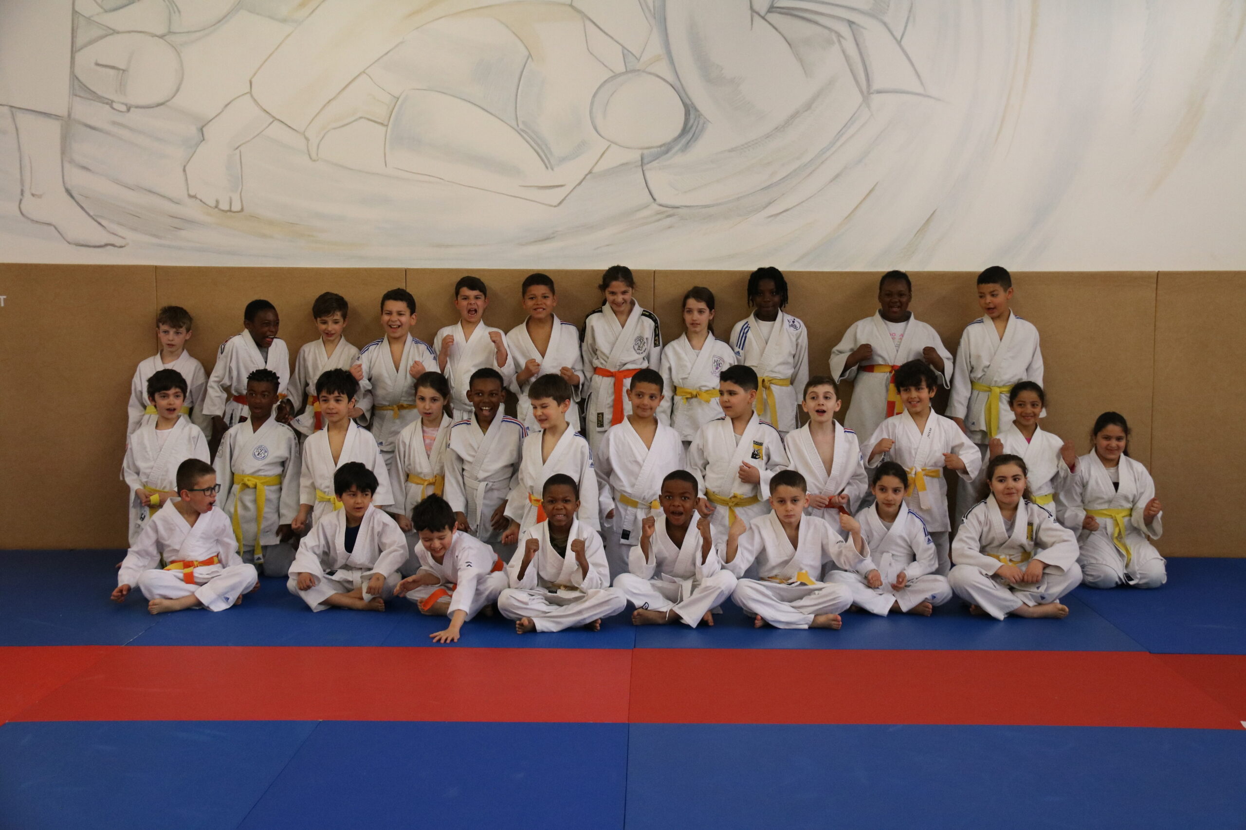 Groupe d'enfants judokas posant fièrement avec leurs ceintures jaunes et blanches après l'entraînement.