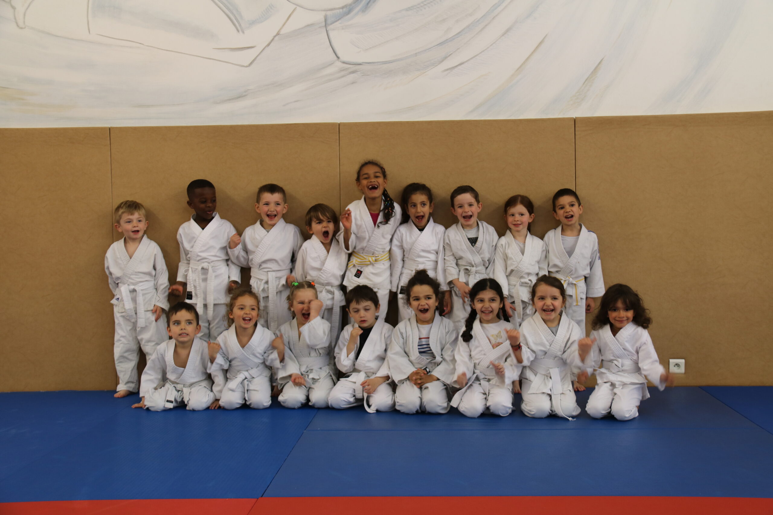 Jeunes judokas en ceinture blanche alignés pour une photo de groupe, exprimant leur enthousiasme.