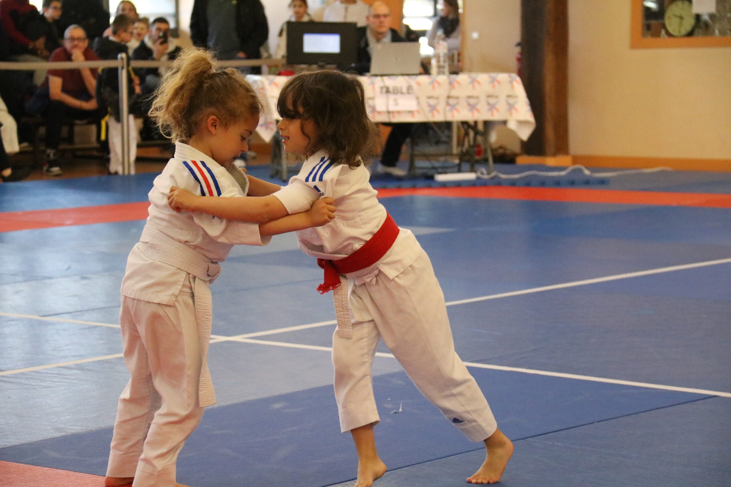 Deux petites judokas s'affrontant avec détermination lors d'un tournoi.