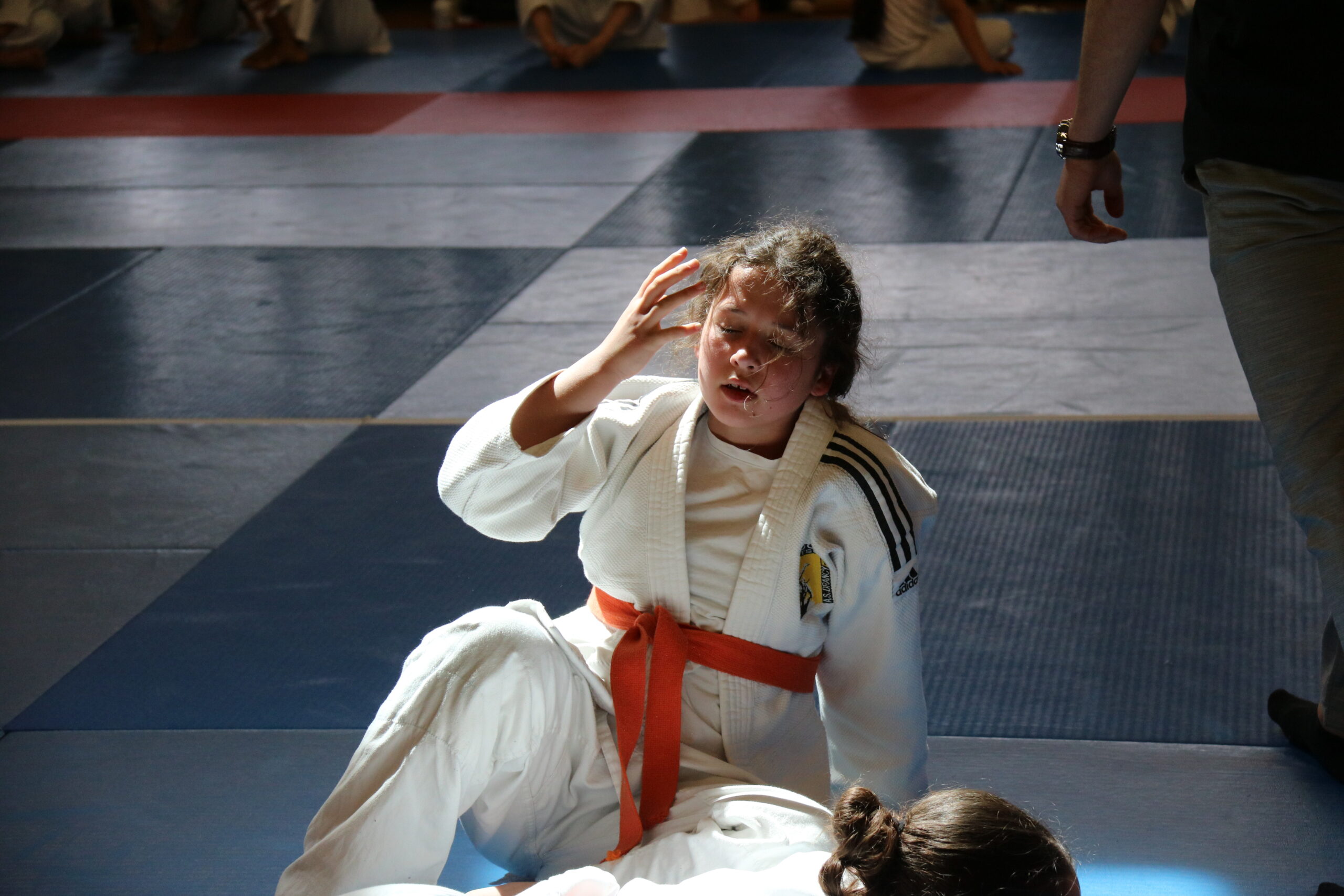 Jeune judoka assise après un combat, se tenant la tête, sous la lumière du tatami.