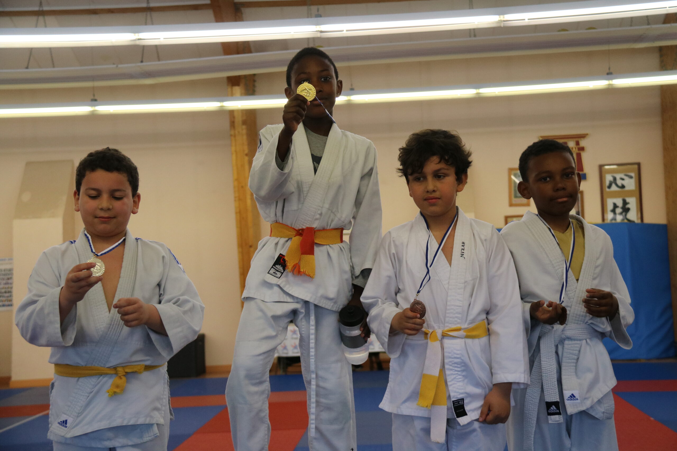 Quatre jeunes judokas fiers de leurs médailles, posant sur le podium après une compétition.