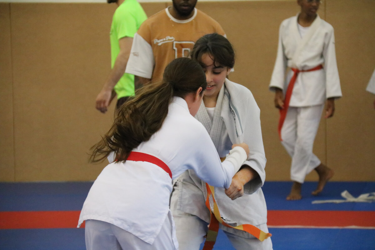 Deux jeunes judokas en ceinture blanche et rouge posant fièrement sur le tatami.