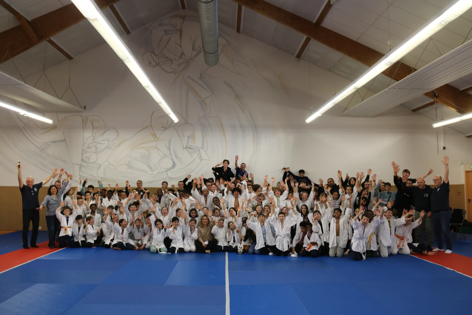 Grande photo de groupe de fin de tournoi : tous les judokas et encadrants réunis, les mains levées pour célébrer.